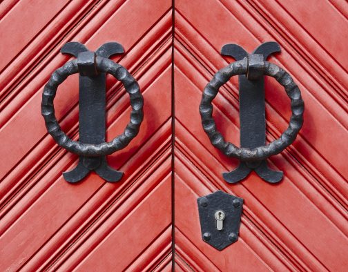 Antique metallic door knob on a red wooden doors. Horizontal